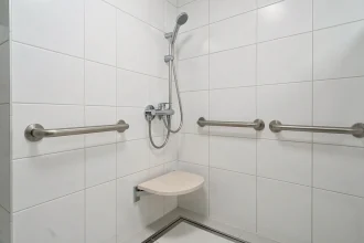 Mitigeur thermostatique douche installé à hauteur PMR avec barre d'appui et siège rabattable dans une salle de bains accessible