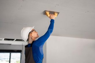 Femme souriante réparant un plafond endommagé avec des outils